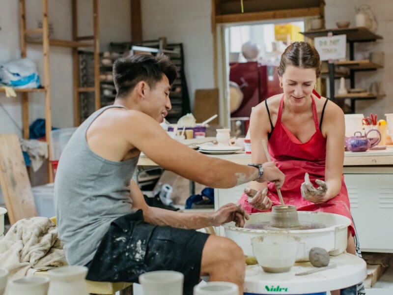 A woman and a man working on a throwing wheel in a pottery class